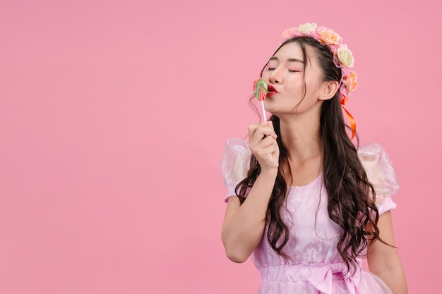 Eine schöne frau, die in einer rosa prinzessin gekleidet wird, spielt mit ihrer süßen süßigkeit auf einem rosa. Kostenlose Fotos