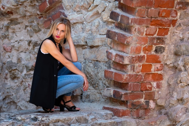 Eine Schone Frau Mit Langen Blonden Haaren Einer Weissen Bluse Und Blauen Jeans An Der Steinmauer Der Altstadt Premium Foto