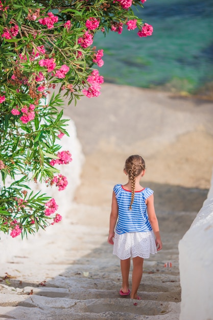 Entzückendes mädchen, das spaß draußen hat. scherzen sie an der straße des typischen griechischen traditionellen dorfs mit weißen wänden und bunten türen auf mykonos-insel, in griechenland Premium Fotos