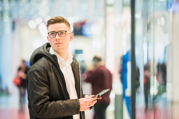 Ernster junger mann, der in der hand die digitale tablette weg schaut hält Kostenlose Fotos