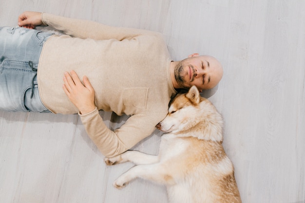 Erwachsener kahler mann mit huskywelpen, der auf boden schläft