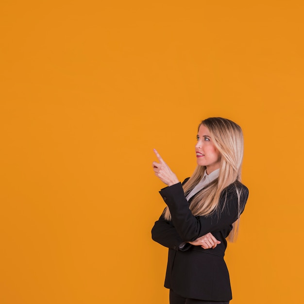 Erwogene junge geschäftsfrau, die ihren finger gegen einen orange hintergrund zeigt Kostenlose Fotos