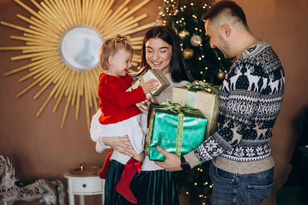 Familie mit kleiner tochter durch den weihnachtsbaum, der geschenkbox auspackt Kostenlose Fotos
