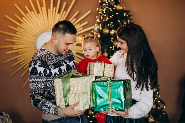 Familie mit kleiner tochter durch den weihnachtsbaum, der geschenkbox auspackt Kostenlose Fotos