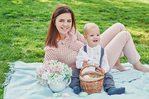 Familienfotosession der mutter und des babysohns für ostern im park, nahe bei ihnen ist ein korb mit eiern und einem ostern-kaninchen Premium Fotos
