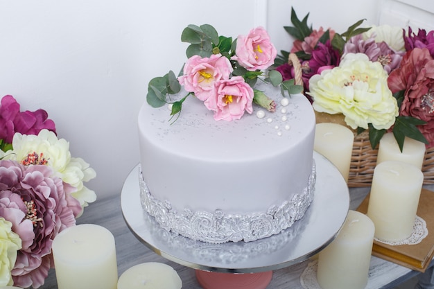 Festlicher kuchen mit mastix wird mit rosa blumen nah oben verziert. schöne leckere torte decoratrd mit rosen am geburtstag oder hochzeitsfeier. schokoriegel auf dem festlichen tisch. Premium Fotos