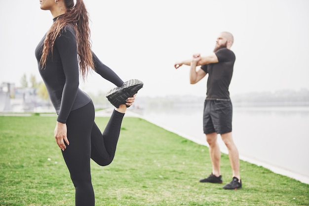 Fitness-paar, das draußen im park nahe dem wasser streckt ...