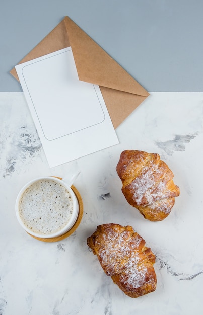 Flache lagezusammensetzung mit tasse kaffee, hörnchen und sauberer leerer anmerkung für text auf hintergrund. Premium Fotos