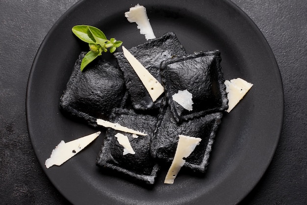 Flache schwarze ravioli auf dunklem teller mit käsescheiben ...