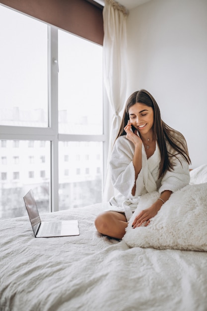 Frau, die an computer im bett arbeitet und am telefon ...