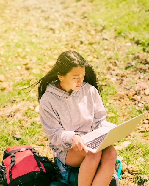 Frau, die auf rucksack sitzt und im laptop arbeitet Kostenlose Fotos