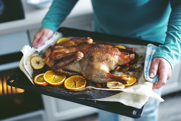 Frau, die ente mit gemüse kocht und es vom ofen setzt. | Premium-Foto