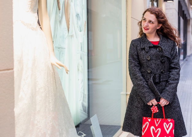 Frau, die hochzeitskleid im shopfenster betrachtet ...