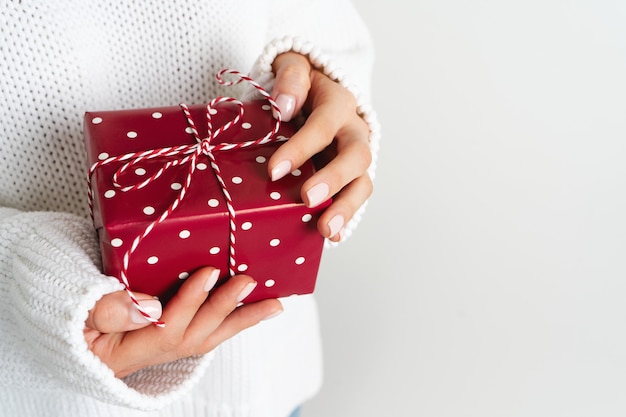 Frau in der woolen weißen strickjacke, die eine geschenkbox mit einem bogen hält. weihnachtsfestliches layout. modell für das neue jahr. Premium Fotos