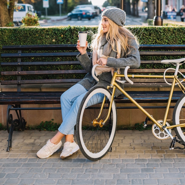 Frau mit cup und fahrrad auf bank | Kostenlose Foto