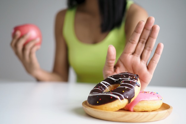 Frauen schieben die donutplatte, die eine mischung aus transfett ist. und entscheide dich, den apfel zu halten. iss kein junk food. diät-konzept Premium Fotos