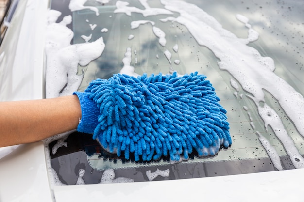 Frauenhand mit dem blauen mikrofasergewebe, das modernes auto des rückspiegels wäscht oder automobil säubert. Premium Fotos