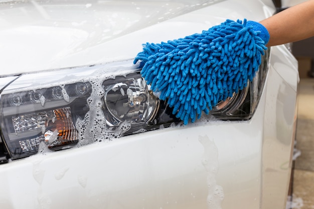 Frauenhand mit modernem auto des blauen mikrofasergewebes waschendem scheinwerfer oder reinigungsautomobil. Premium Fotos