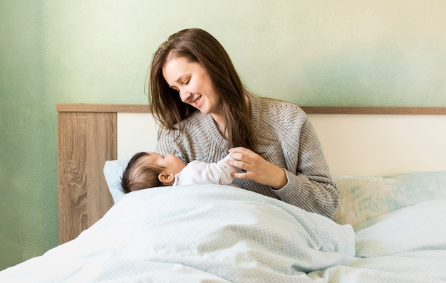 Frohe mutter, die baby in den armen im bett hält ...