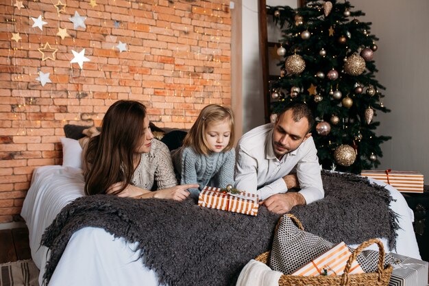 Frohe weihnachten und schöne feiertage! nette eltern und ihr nettes tochtermädchen, die zu hause geschenke auf bett austauschen. Premium Fotos