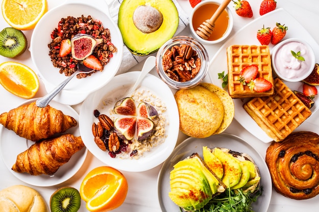 Frühstückstisch mit avocadotoast, hafermehl, waffeln, hörnchen auf weiß Premium Fotos