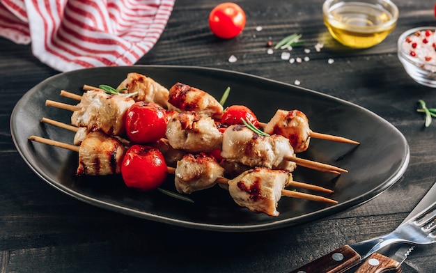 Gegrillte hähnchen-spieße mit kirschtomaten auf einem schwarzen teller ...