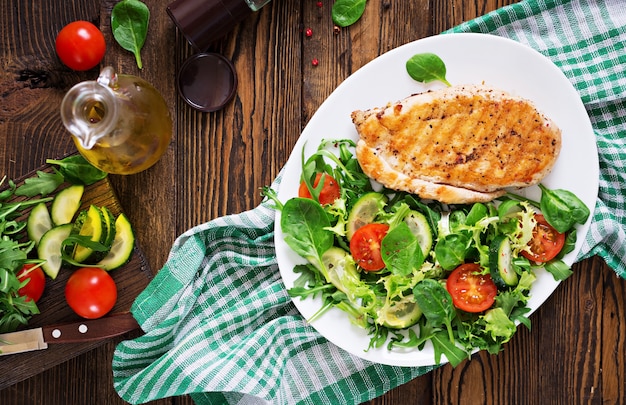 Gegrillte hähnchenbrust und frischer gemüsesalat - tomaten, gurken und salatblätter. hühnchensalat. gesundes essen. flach liegen. ansicht von oben Kostenlose Fotos