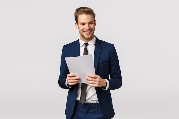 Geschäfts-, eleganz- und erfolgskonzept. hübscher stilvoller moderner geschäftsmann im klassischen anzug, bindung, dokumente verwahrend, papier und das lachen, lächelnd schauen weg, drücken vertrauen, weißer hintergrund aus Premium Fotos