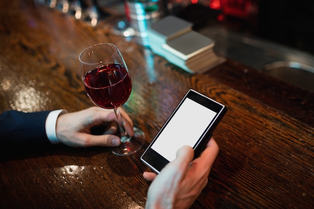 Geschäftsmann, der handy mit glas rotwein in der hand