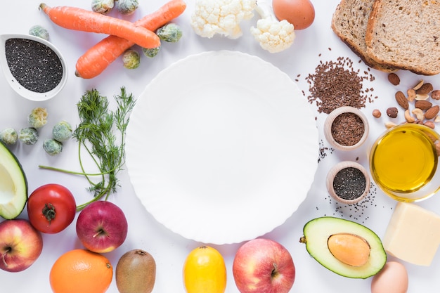 Gesunde früchte; gemüse; trockenfrüchte; brot; samen und käse; ei; öl; mit leerer platte über weißem hintergrund Kostenlose Fotos
