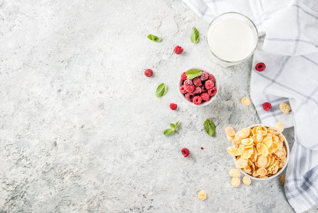 Gesunde frühstückszutaten. frühstückskost aus getreide blättert milch- oder joghurtglashimbeeren und -minze auf grauem steinhintergrund ab Premium Fotos