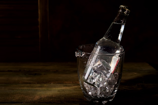 Glas-eiskübel mit einer flasche tonikum, rum oder anderem alkohol auf dunklem holz backgorund Premium Fotos