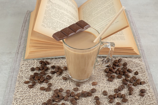 Glas kaffee mit schokolade, buch und kaffeebohnen auf