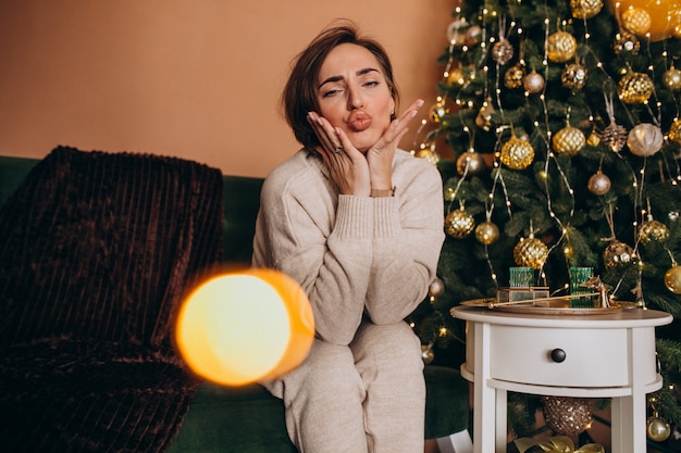 Glückliche frau, die auf sofa durch den weihnachtsbaum sitzt Kostenlose Fotos