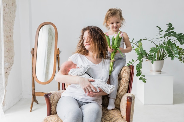 Glückliche mutter, die auf sessel mit ihrem netten kind zwei im haus sitzt Kostenlose Fotos
