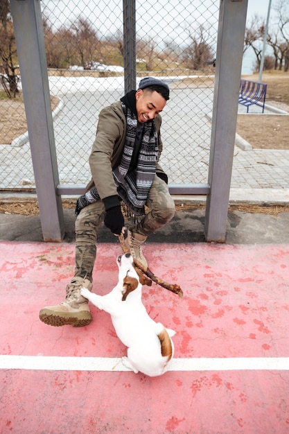 Glücklicher afrikanischer mann, der lächelt und mit hund draußen spielt