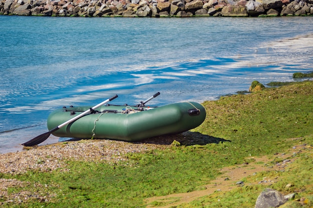 Gummiboot mit der fischereiausrüstung, die auf einem fluss nahe dem sandigen strand steht. Premium Fotos