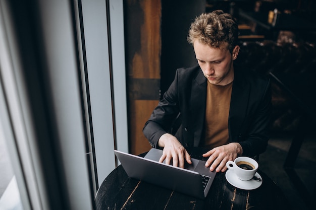 Gut aussehender mann, der an einem computer in einem café arbeitet und kaffee trinkt Kostenlose Fotos