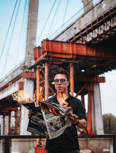 Guy liest eine brennende zeitung vor einer brücke Kostenlose Fotos