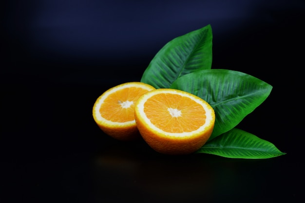 Halbe reife orange frucht nützlich mit blatt auf einem lokalisierten schwarzen hintergrund Premium Fotos