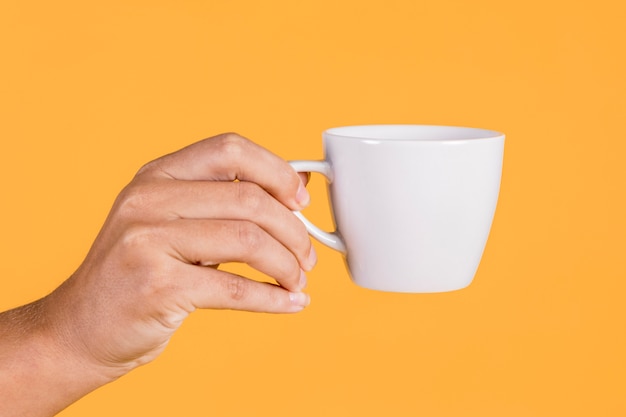 Hand der person, die kaffeetasse gegen farbigen hintergrund hält Kostenlose Fotos
