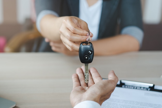 Hand des vertreters, der dem kunden autoschlüssel nach unterzeichnetem mietvertragsformular gibt. Premium Fotos