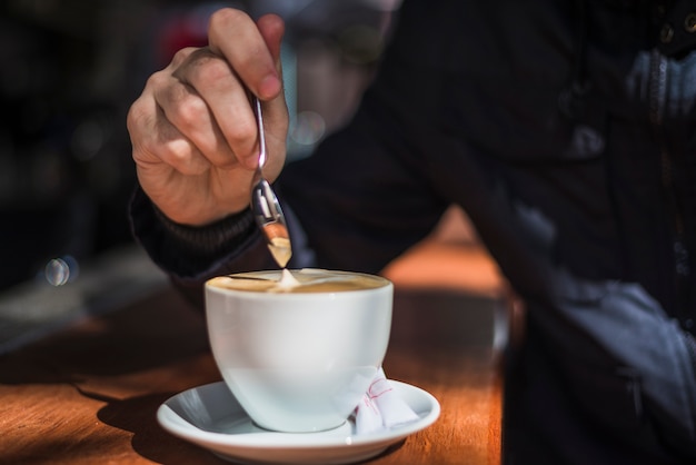 Handkaffee einer person, die lattekaffee mit löffel in der weißen kaffeetasse auf holztisch rührt Kostenlose Fotos
