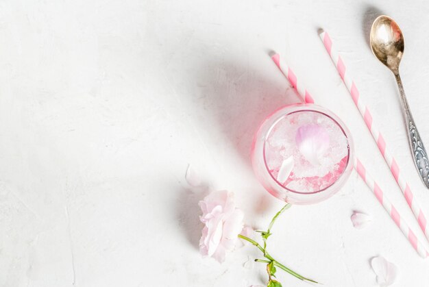 Hellrosa rosencocktail, mit roséwein, rosafarbenen blumenblättern des tees und zitrone auf einer weißen konkreten steintabelle. Premium Fotos