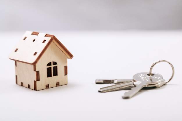 Hölzernes miniaturhaus mit türschlüsseln schließen oben. immobilien-konzept. kleines spielzeugholzhaus mit schlüsseln mit kopienraum Premium Fotos