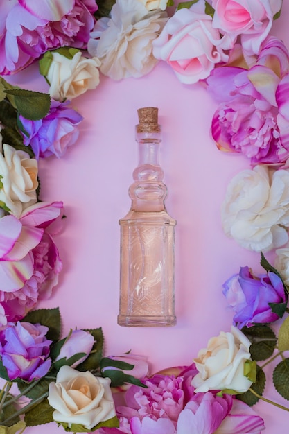 Hohe winkelsicht des ätherischen öls umgeben mit frischen blumen auf rosa hintergrund Kostenlose Fotos