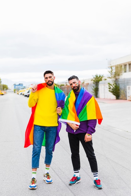 Homosexuelle paare, die mit regenbogenflagge auf straße ...