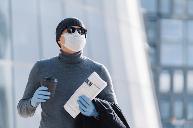 Horizontale Aufnahme Des Jungen Mannes In Der Medizinischen Maske Verhindert Infektiose Lungenentzundung Coronavirus Pandemie Virus Epidemie Trinkt Kaffee Zum Mitnehmen Zur Arbeit Gehen Posiert Draussen Hat Nachdenklichen Ausdruck Premium Foto