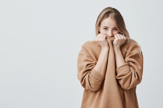 Hubsche Frau Mit Hellem Glattem Haar Und Dunklen Ansprechenden Augen Die Ihr Gesicht In Einem Warmen Losen Pullover Verstecken Kostenlose Foto