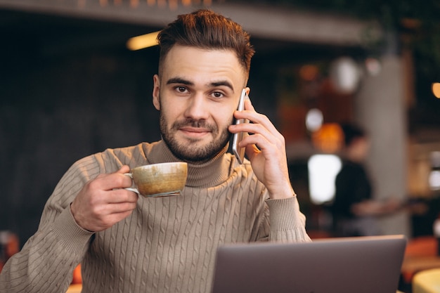 Hübscher geschäftsmann, der an computer arbeitet und kaffee in einem café trinkt Kostenlose Fotos
